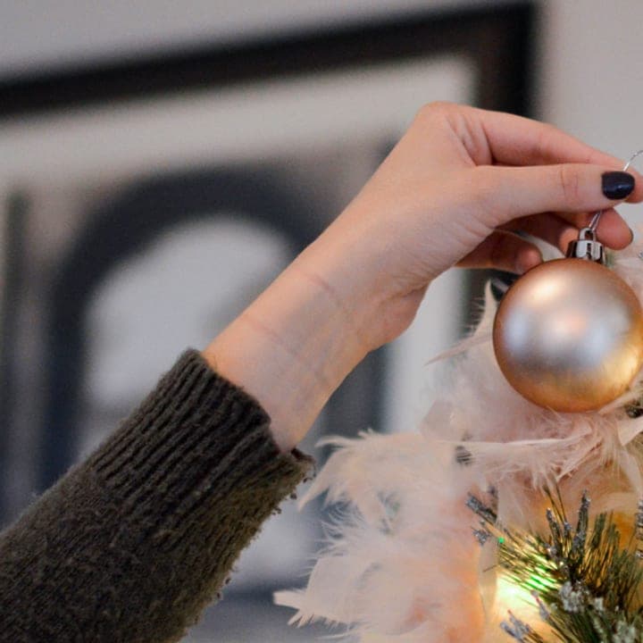 A hand hangs a gold ornament on a frosted tree.